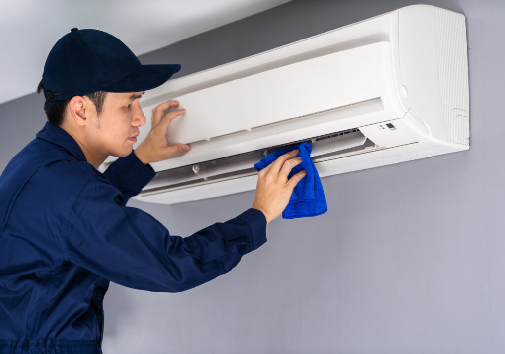 A man cleaning an air conditioner unit with a cloth.