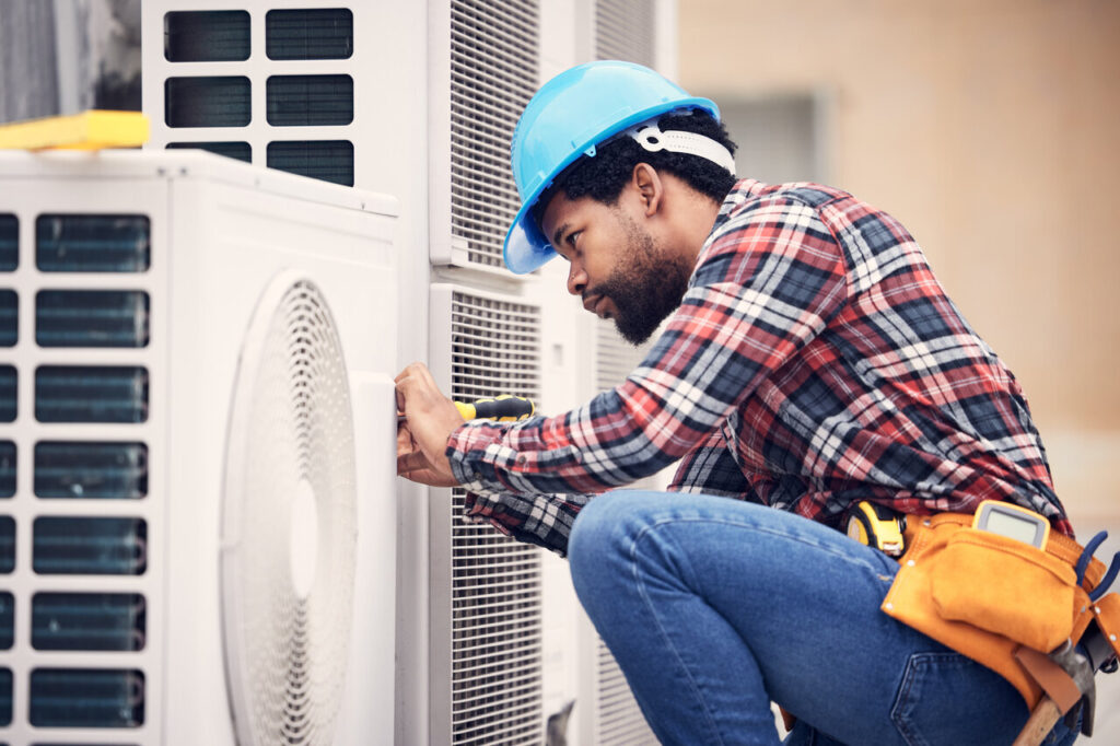 A man in a hard hat and safety vest repairs an air conditioner.