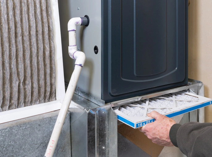 A man cleans a furnace using a filter to improve its efficiency.